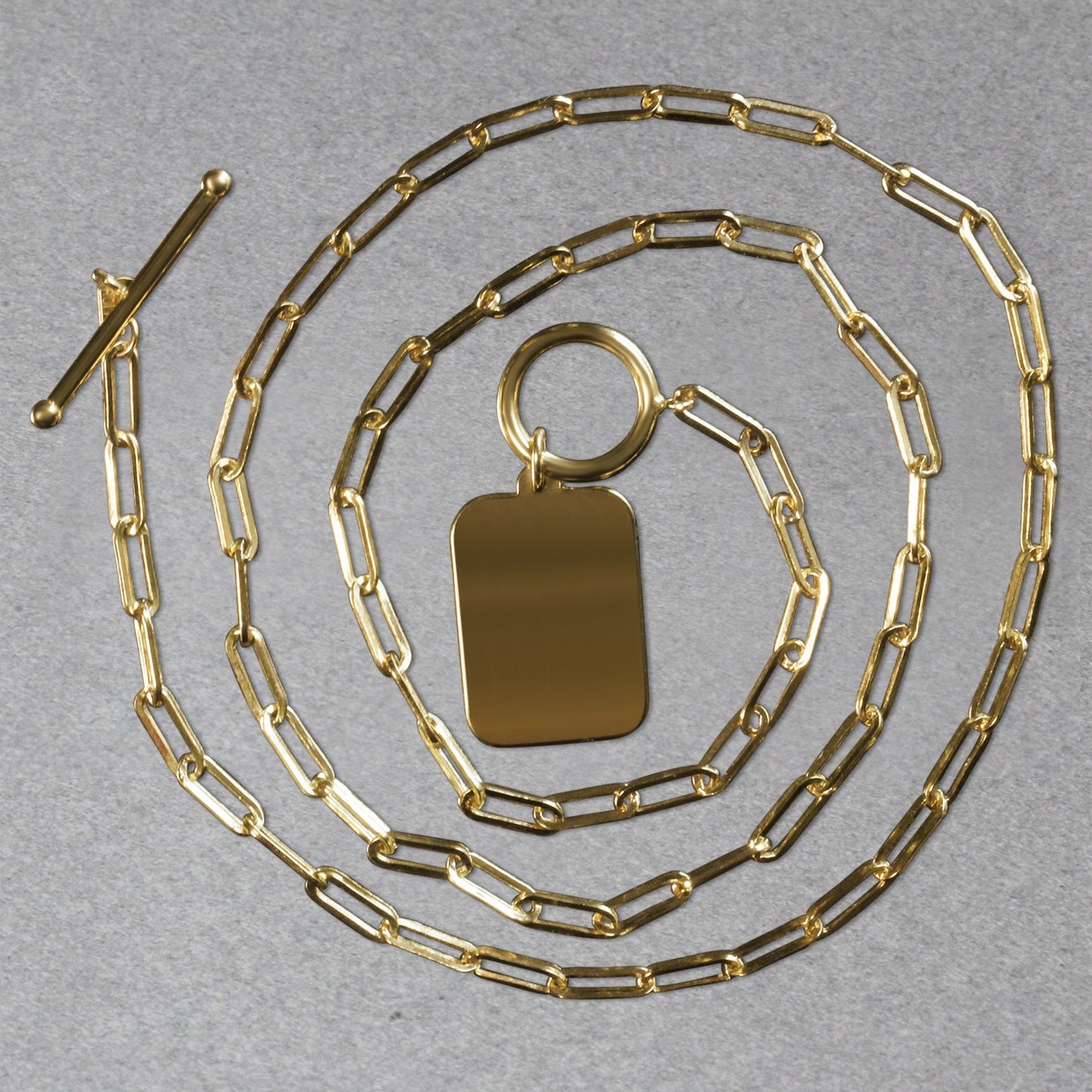 Gold chain necklace with a rectangular pendant on a gray background