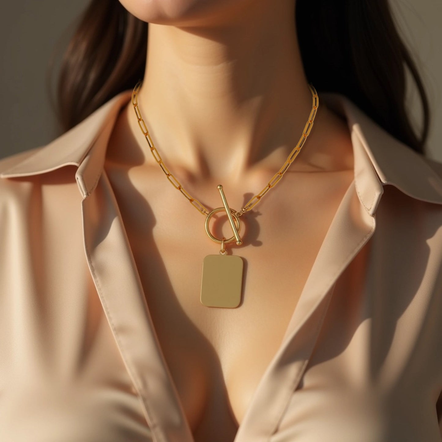 Gold necklace with a pendant worn by a person in a beige shirt.