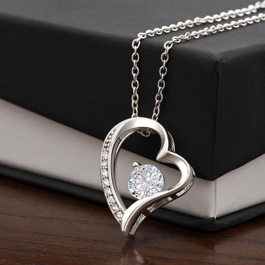 Heart-shaped Forever Love Necklace with a cubic zirconia centerpiece, available in 14K white gold or 18K yellow gold finish, displayed on a black and white gift box.