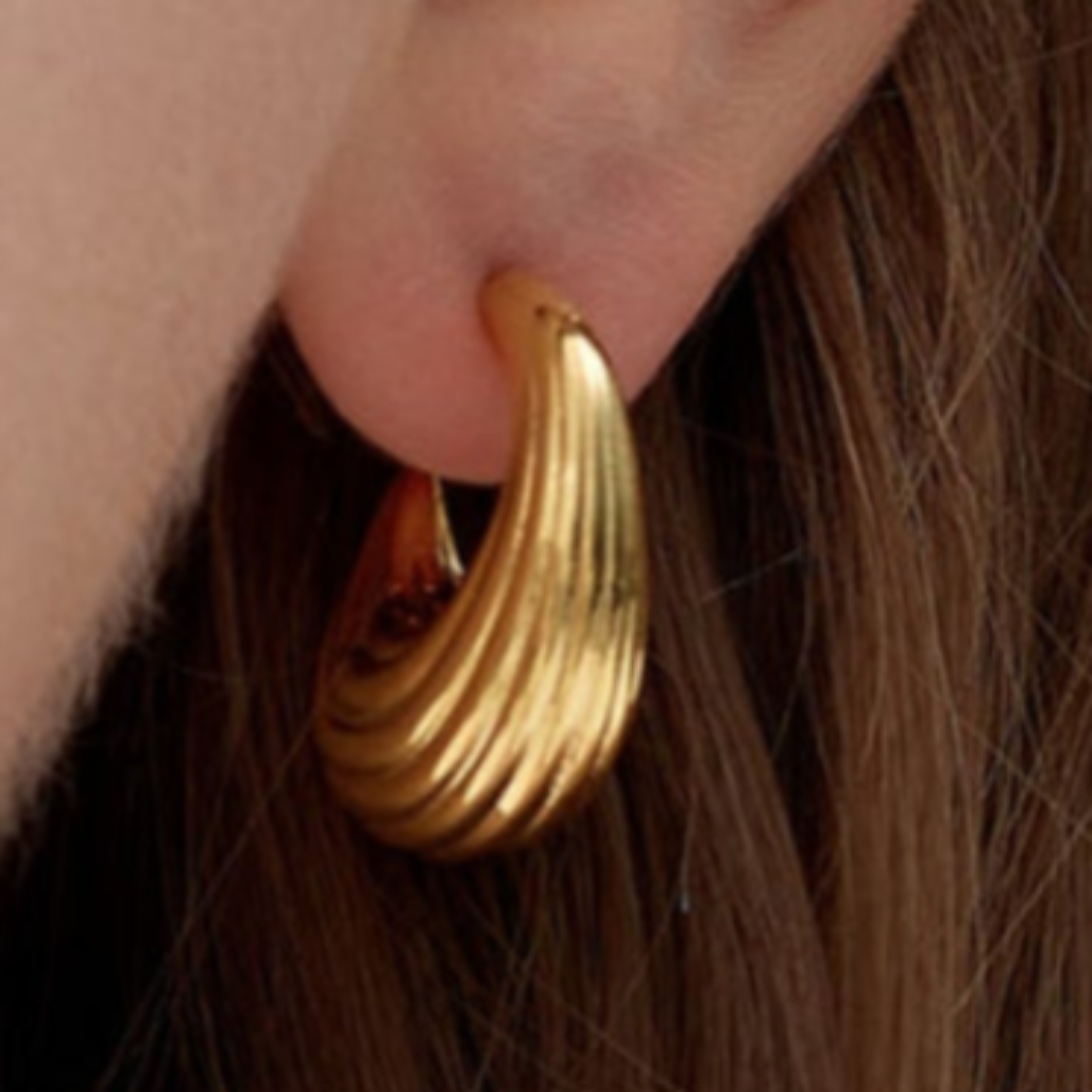 Stylish gold-tone twisted hoop earring with a sleek, modern aesthetic, worn on a woman's ear.