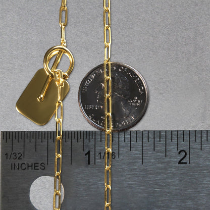 Gold chain with a tag and clasp next to a ruler for size reference on a gray background