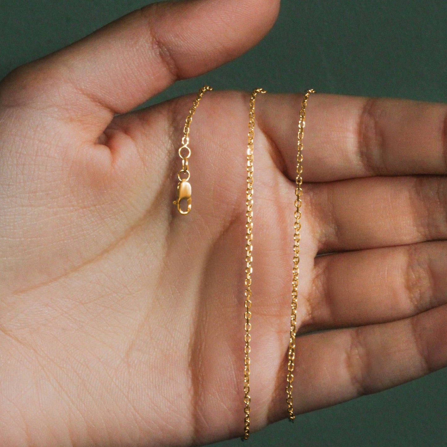 18k Yellow Gold Diamond Cut Cable Link Chain (1.50 mm) held between fingers against a green background