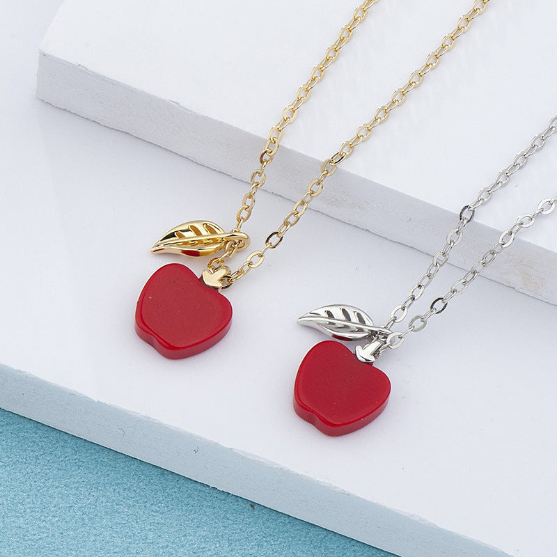 Two necklaces with red apple pendants on a white surface