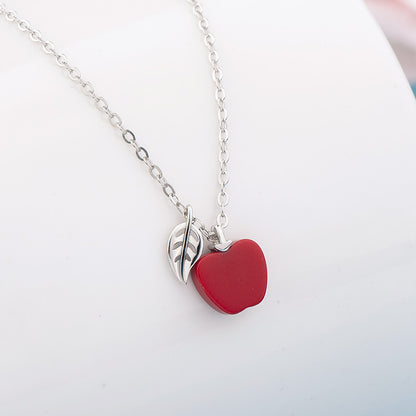 Necklace with a red heart pendant and silver leaf charm on a light gray background