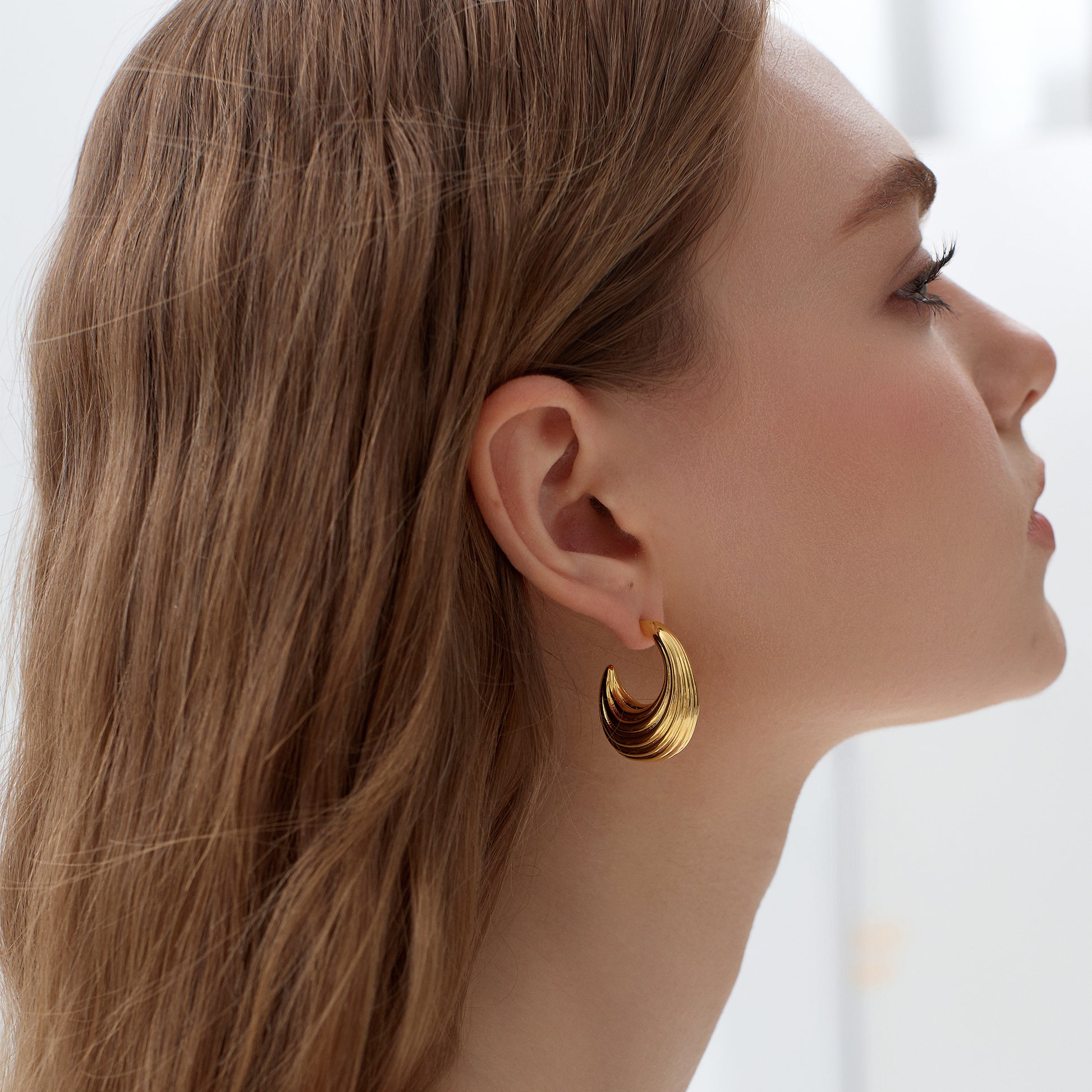Close-up of a woman wearing gold hoop earrings with a blurred background