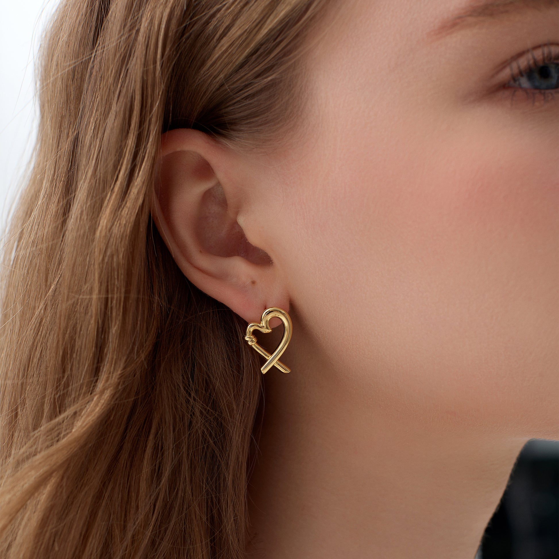 Gold heart-shaped earring worn by a person with blonde hair.
