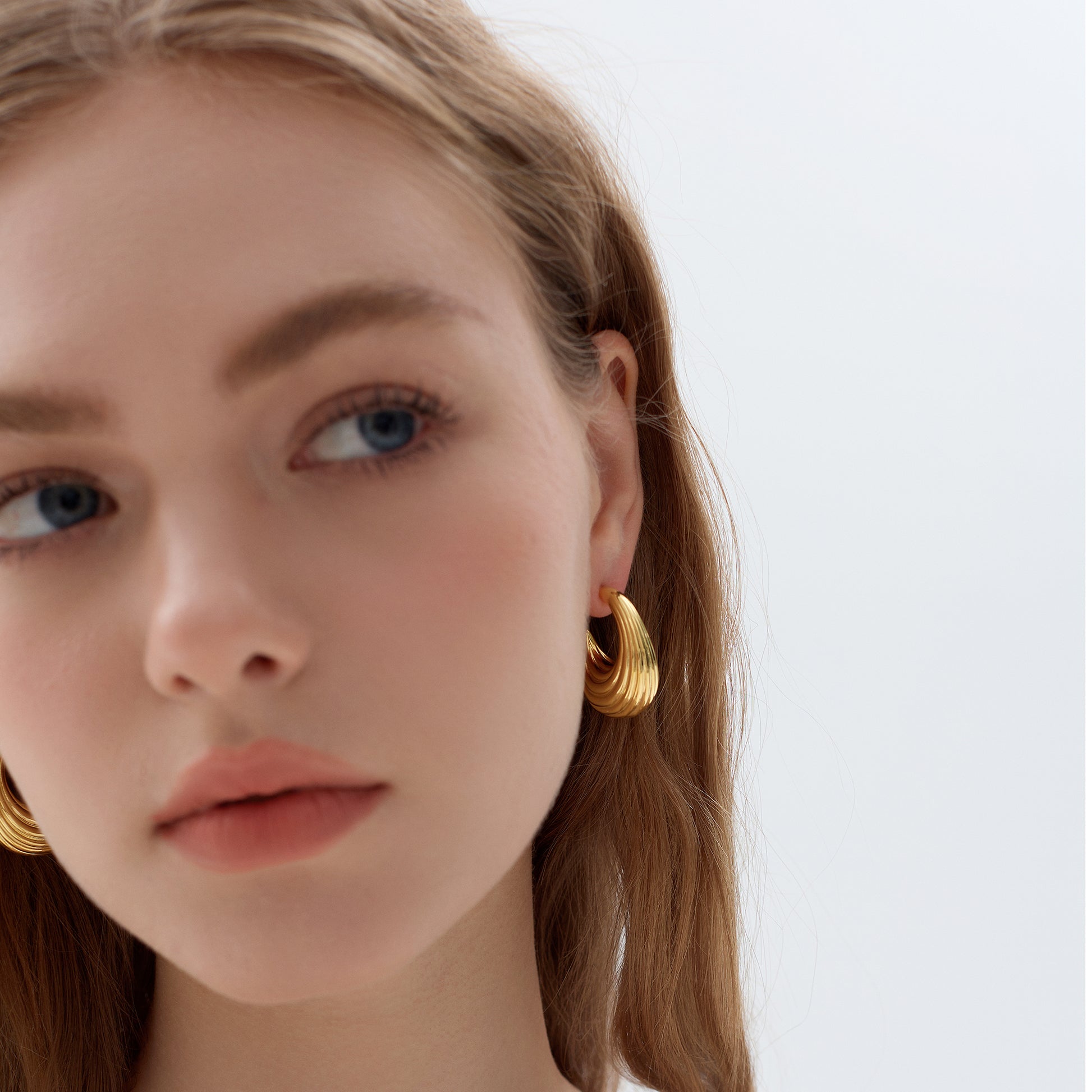Close-up of a person wearing gold hoop earrings with a plain background