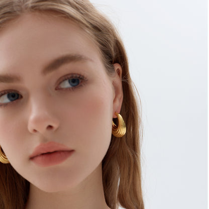 Close-up of a person wearing gold hoop earrings with a plain background