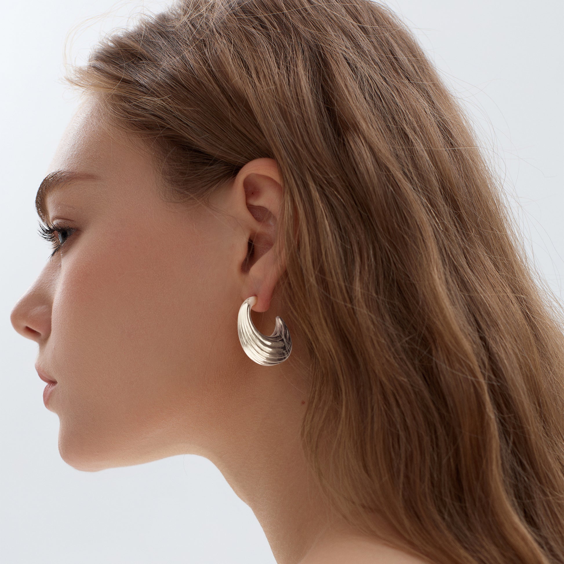 Close-up of a woman wearing gold hoop earrings against a neutral background