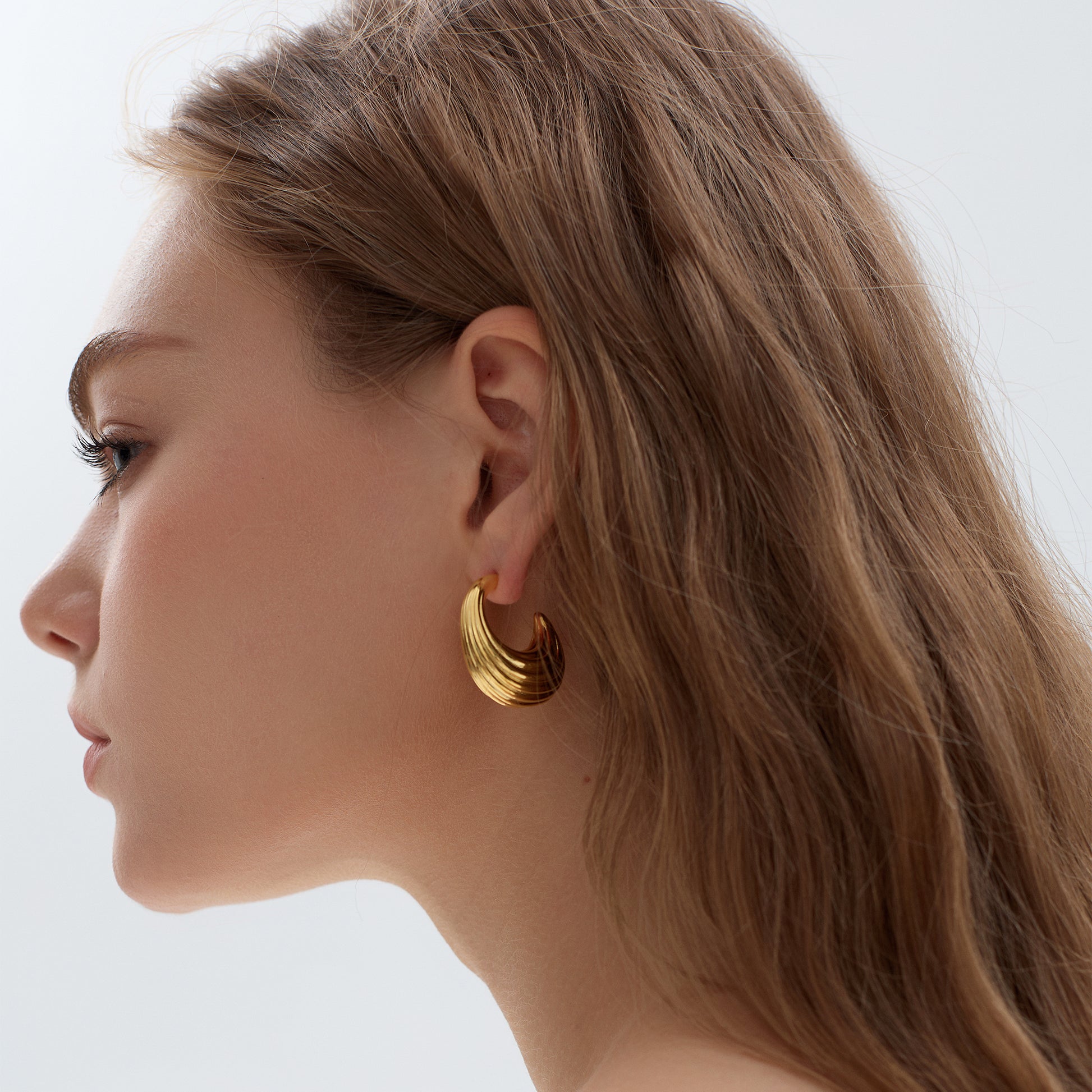 Close-up of a woman wearing gold hoop earrings with a plain background