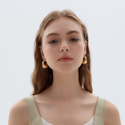 Woman wearing gold hoop earrings against a plain background
