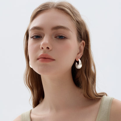 Close-up of a person wearing a silver earring on a plain background