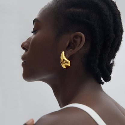 Woman wearing a gold earring against a neutral background