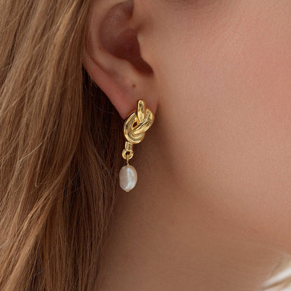 Elegant gold-plated knot and pearl drop earrings with a textured finish, styled on an ear.