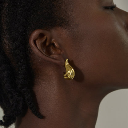 Close-up of a sculpted gold flame-shaped earring on a woman’s ear, exuding bold elegance.