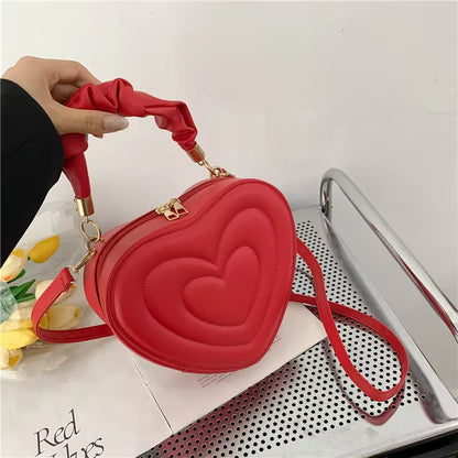 Trendy red heart-shaped PU leather handbag with ruched handle and crossbody strap, perfect for stylish women.